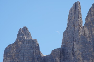 The moon rises in a blue sky above a rocky mountain ridge