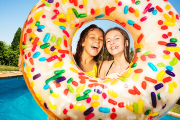 Two friends, young girls stand together with inflatable buoy doughnut on the border of swimming pool