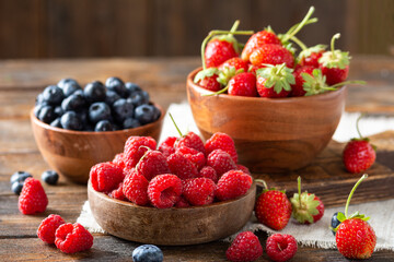 Berries. Various berries in wooden bowls on a brown wooden table. Strawberries, raspberries and blueberries in bowls	