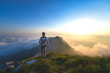 Mountain runner training at sunset with clouds below