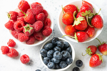 Ripe berries. Different berries in white ceramic bowls on a light table. Strawberries, raspberries and blueberries in plates