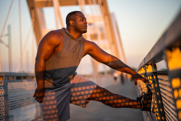 Young african-american man is exercising in sunset on the bridge in the city.