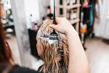 Hairdresser is dyeing female hair, making hair highlights to his client with a foil.