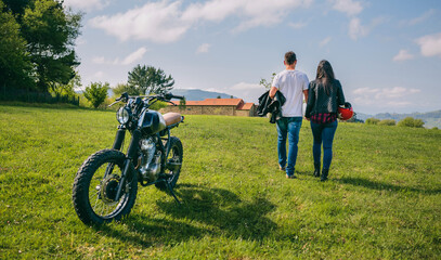 Unrecognizable couple walking on the field holding hands and parked motorbike
