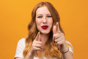 Obraz premium Excited girl with wavy redhead holding fingers in a finger gun gesture and aims at the camera