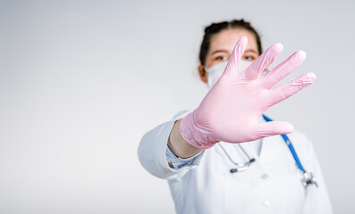 Young woman doctor in a white coat and pink sterile gloves close up shows a stop gesture on white...