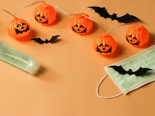Halloween pumpkin lights , black paper bats,medical mask and alcohol sanitizer gel on orange...