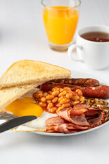 Typical English breakfast with fried eggs, sausages, bacon, beans, mushrooms, orange juice, toasts and tea on the table. Copy space