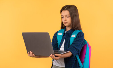 Bored school girl holding laptop at yellow studio