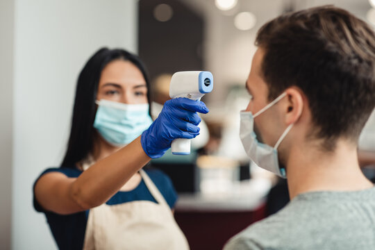Hairdresser checking body temperature of client at barber shop - Powered by Adobe
