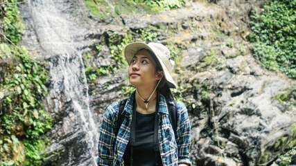 Young girl tourist traveling backpack enjoying adventure exploring nature jungle trail tracking into forest reaching waterfall, wearing travel gear hat and camera,lifestyle.selective focus.