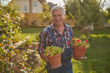 Smiley man holding two flowerpots in the garden