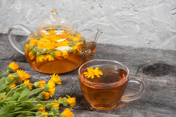 Cup of herbal tea and transparent teapot and marigold flowers on wood background. Calendula Tea Benefits Your Health concept. Copy space