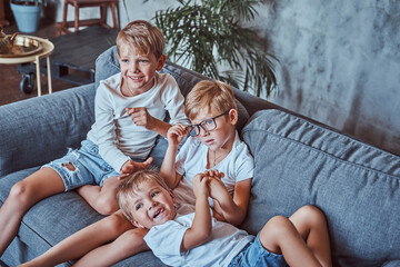 Joyful children from one american family sitting on sofa and playing with each other at home.
