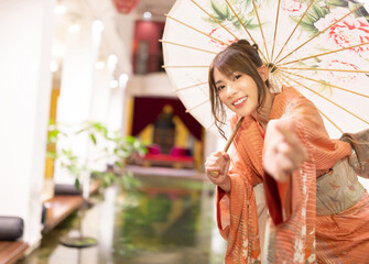 Asian beautiful woman in traditional Japanese kimono with an umbrella  and smiling at camera,...