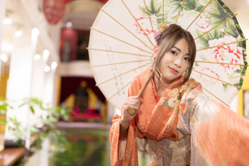 Asian beautiful woman in traditional Japanese kimono with an umbrella  and smiling at camera,...