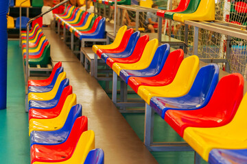 Fototapeta na wymiar Multicolored Empty plastic chairs in the stands of the stadium. Many empty seats for spectators in the stands. Empty plastic chairs for football fans in the gym. Bright colorful seats for stadium fans