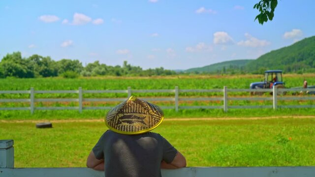 back view unrecognizable farmer looking on the agricultural field tractor working in the field harvest time farming concept