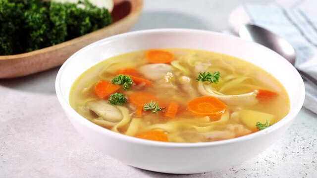 Homemade chicken soup with noodles and vegetables in white bowl, white background. Healthy warm comfortable food.