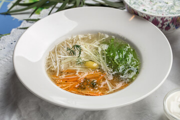 chicken broth with egg with carrot and cabbage on white plate on the table at restaurant