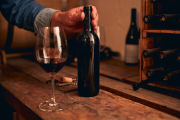 Hand touching unlabeled bottle of red wine