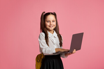 E-education. Smiling schoolgirl in uniform with backpack works on laptop