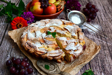 Apple pie sprinkled with icing sugar on a wooden background. Seasonal homemade baked goods.