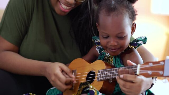 Happy Mom with her daughter playing guitar and singing together at home, happy family