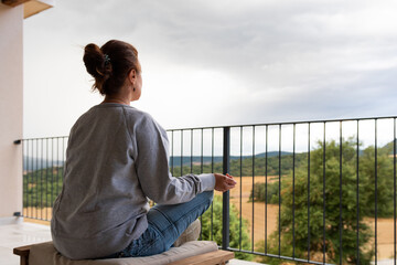 Mujer sentada meditando en el balcón del hogar con las piernas recogidas y los brazos extendidos
