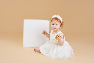 Little red-haired baby girl is playing on a beige background. Big mole on the forehead, not like everyone else