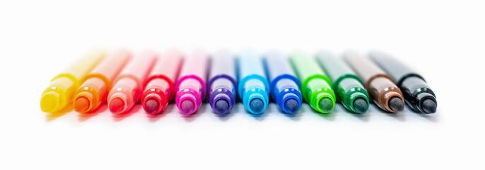 A set of multi-colored felt-tip pens in a row, rainbow on a light white banner background close-up. Drawing markers, pencils, ink, artist tools, creativity, leisure, hobby. Colorful school supplies.