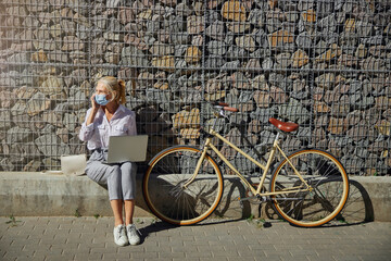 Fototapeta na wymiar Woman wearing protective mask with laptop and bicycle in the outdoors