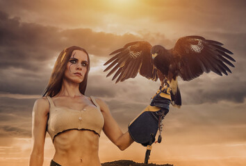 Beautiful woman posing on nature with eagle against cloudy sunset sky