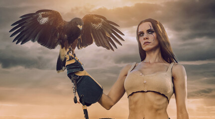 Beautiful woman posing on nature with eagle against cloudy sunset sky