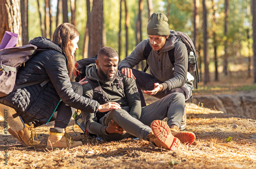 Wall mural friends helping african injured guy while hiking by forest