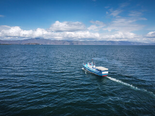 Naklejka premium Aerial view of a steamboat, A fishing ship in the middle of a lake with beautiful coastline behind