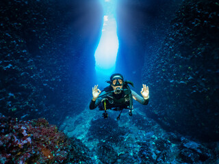 Eine Scuba Taucherin signalisiert das OK Zeichen vor einer Unterwasser Höhle im Ägäischen Meer,...