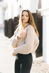 Portrait of a young beautiful fashionable girl in a knitted beige sweater, posing on the street of a European city.