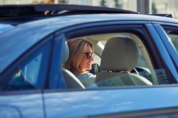 Happy attractive caucasian woman, business lady wearing eyeglasses driving her modern car and smiling