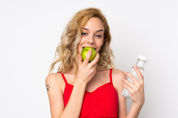 Young blonde woman isolated on white background with a bottle of water and eating an apple