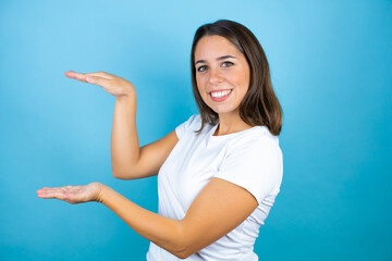 Young beautiful woman over isolated blue background gesturing with hands showing big and large size sign, measure symbol. Smiling looking at the camera. Measuring concept.