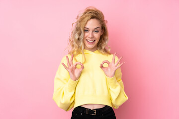 Fototapeta na wymiar Young blonde woman wearing a sweatshirt isolated on pink background showing an ok sign with fingers