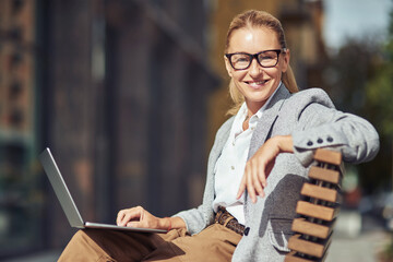 Beautiful succesful middle aged business woman wearing eyeglases sitting on the bench outdoors and...