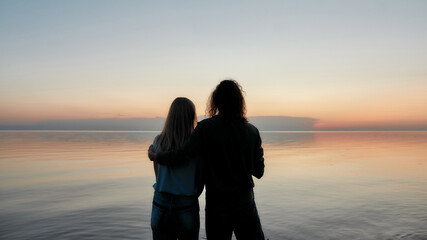 Fototapeta premium Silhouetted couple embracing while watching beautiful sunset on the river together