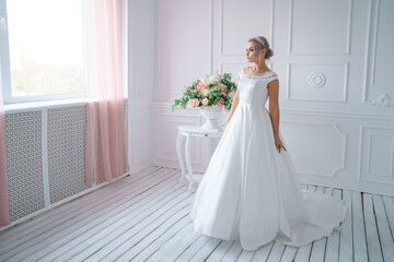 Fototapeta na wymiar A young bride stands against the background of a white room.