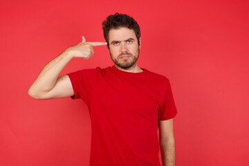 Unhappy  Young handsome caucasian man wearing t-shirt over isolated red wall makes suicide gesture...