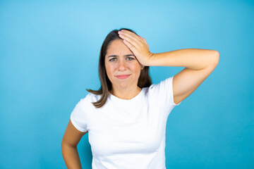 Young beautiful woman over isolated blue background putting one hand on her head smiling like she had forgotten something