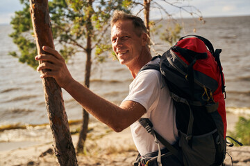 Jolly athletic male walking with backpack in nature