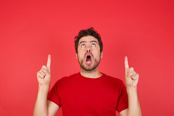 Young handsome caucasian man wearing t-shirt over isolated red background amazed and surprised...
