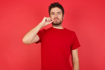 Young handsome caucasian man wearing t-shirt over isolated red background mouth and lips shut as...
